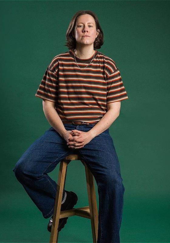Chloe Petts sitting on a stool wearing jeans and a striped top