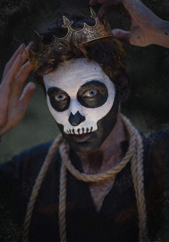 Close-up of a man with his face painted like a skeleton, wearing a rope around his neck and a crown on his head.
