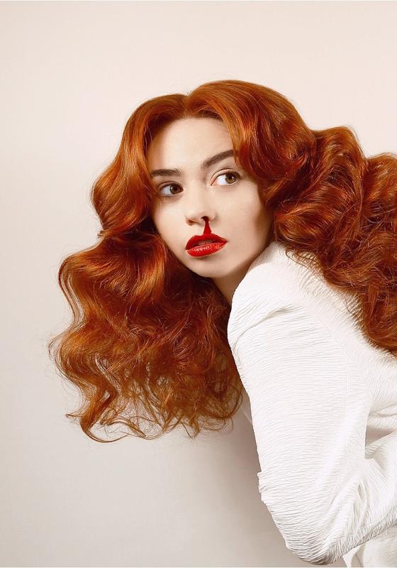 Hannah's gorgeous red hair cascades down as they look out with an arm twisted behind their back and bloody nose which is the same shade as their lipstick.