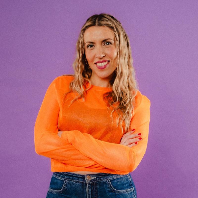 Lou smiling at the camera wearing an orange top on a purple background.