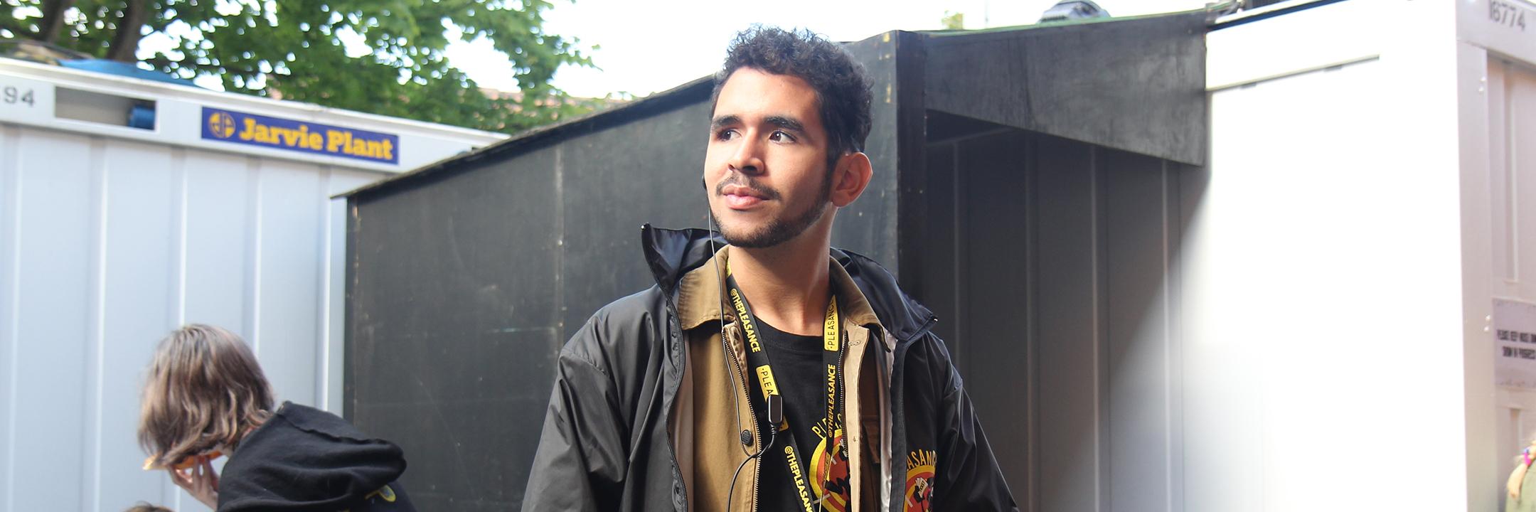 A confident Pleasance team member sports their uniform, radio and earpiece proudly stood against the doorway of their venue.