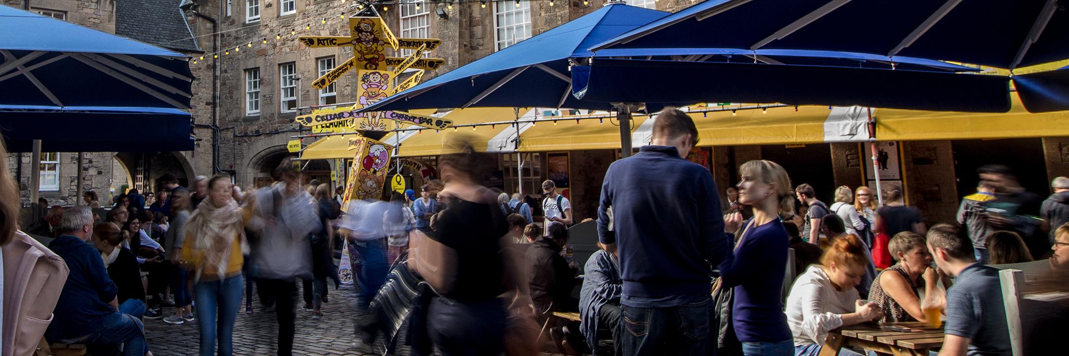 Bustling image of the courtyard with blue umbrellas and people sitting at picnic tables.