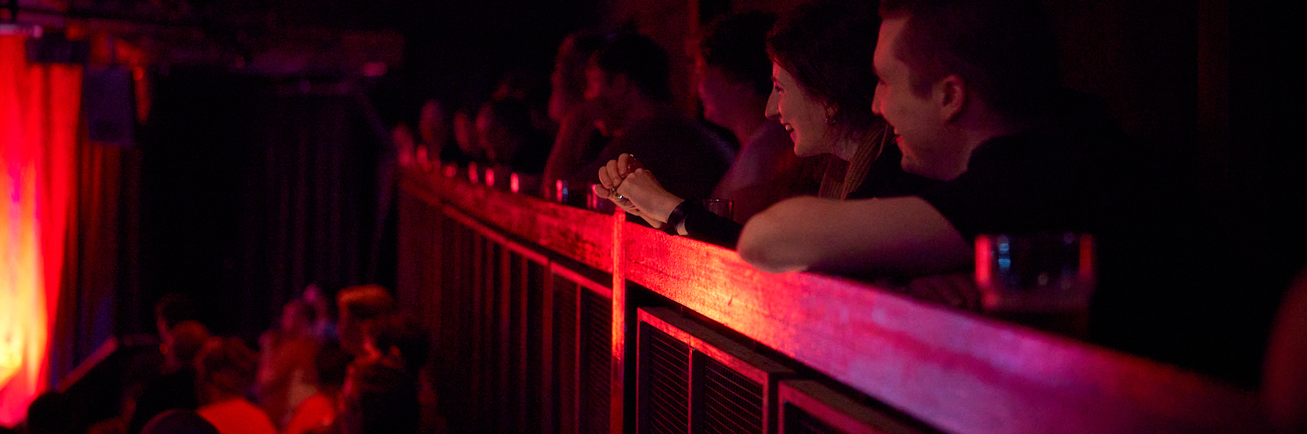 A group of people lean over the Pleasance's balcony laughing, facing towards the stage