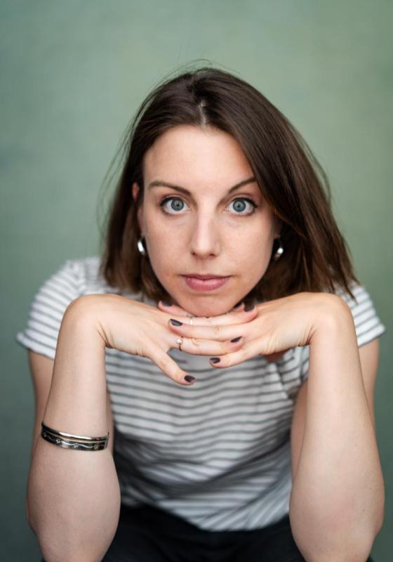 A headshot of Isobel as she looks directly into the camera. Her head is resting on her hands and she is wearing a striped t-shirt and silver jewelry. 