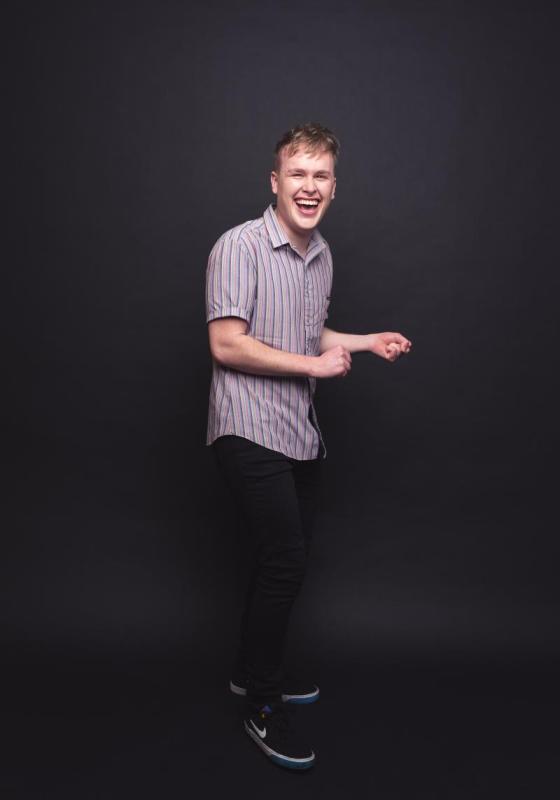 Full length photo of Josh with cheeky smile wearing a striped short-sleeve shirt.