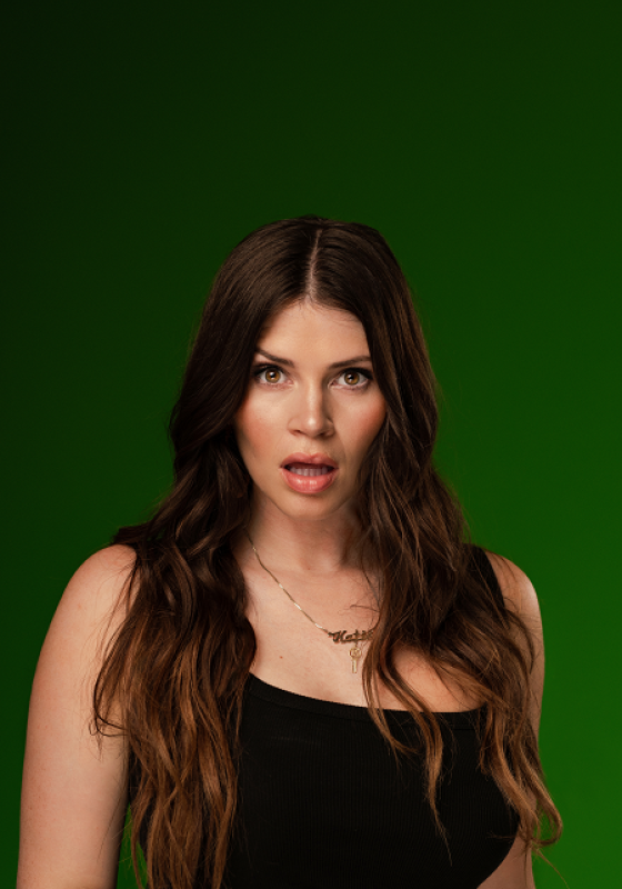 Woman stands in front of green backdrop with her mouth agape in a shocked expression