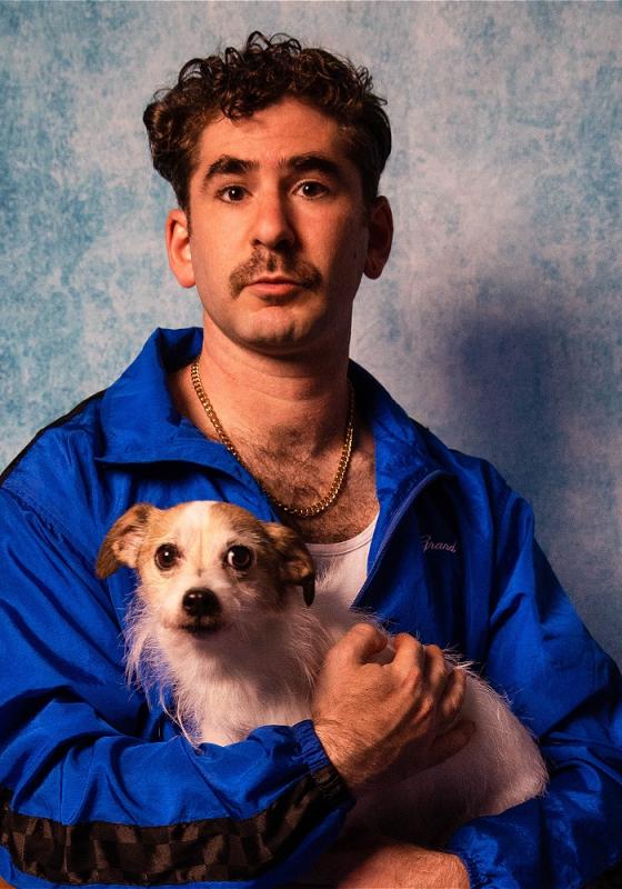 Josh Glanc in an 80s-esque school photo holding a dog and looking directly at the viewer.