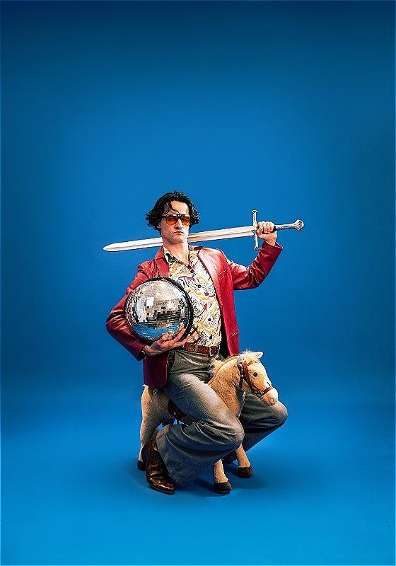 Jazz sitting on a small toy horse, holding a disco ball & a sword. 