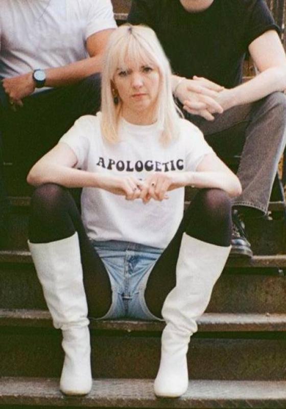 Woman sitting on stairs with white t shirt on that says APOLOGETIC with two figures sitting behind her