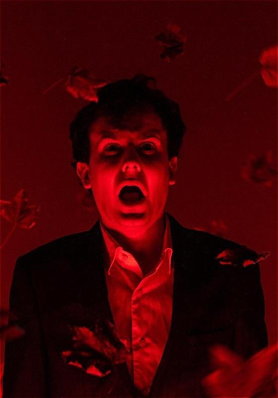 Andrew wears a suit with an expression of horror with harsh red lighting.