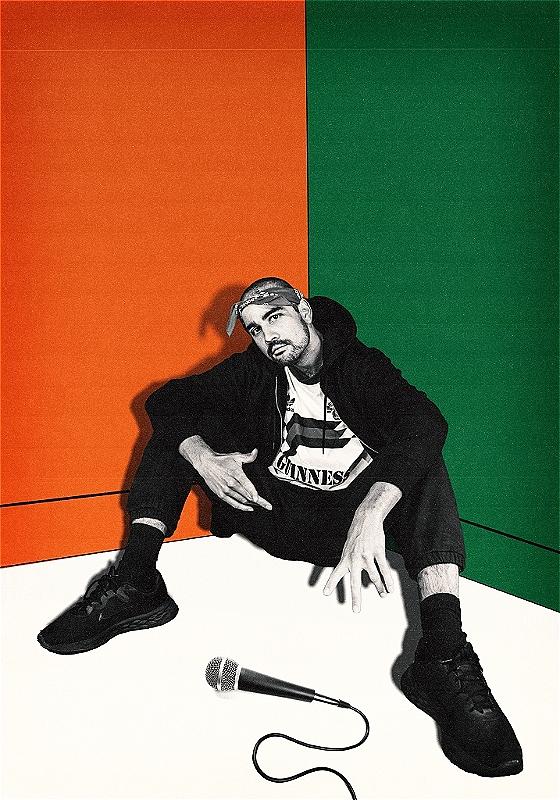 The performer sits in a corner in black and white. The walls behind him painted green, orange and white to represent the Indian flag. A microphone lies on the floor.
