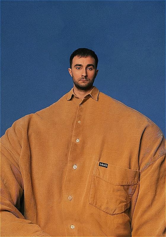 Eddie wears a comically oversized yellow shirt against a blue background.