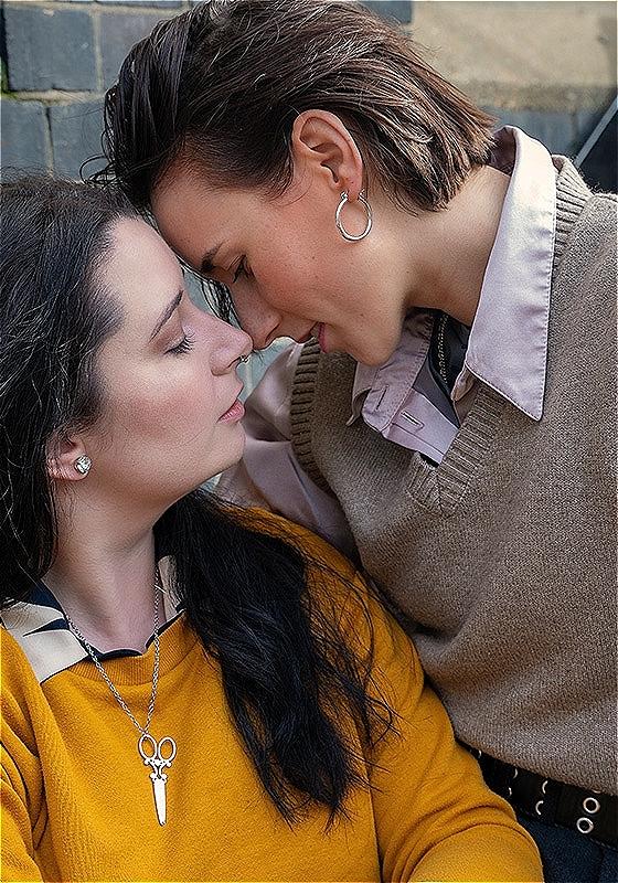 Two woman stand with their faces tilted towards each other, about to embrace.