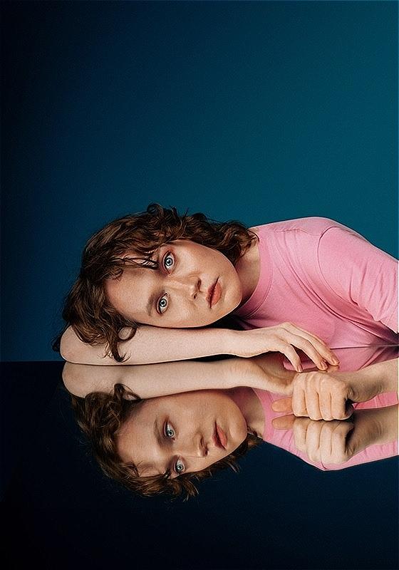 The performer lays looking into the camera with her reflection seen underneath her.