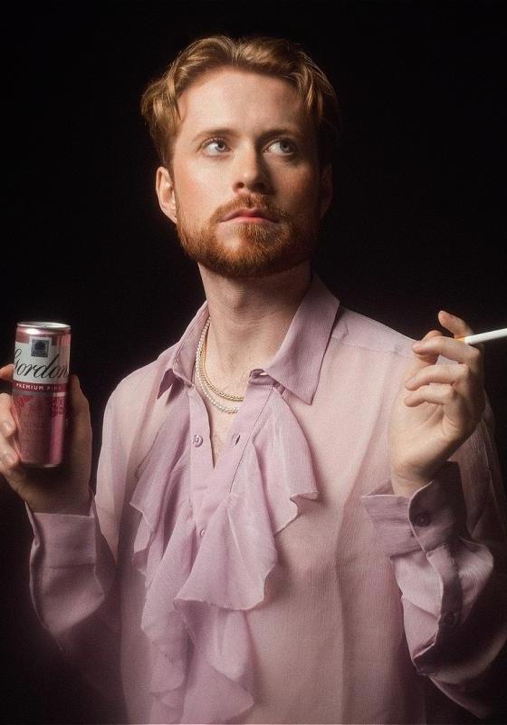 John gazes into the distance holding a cigarette and a can of pink gin and tonic.