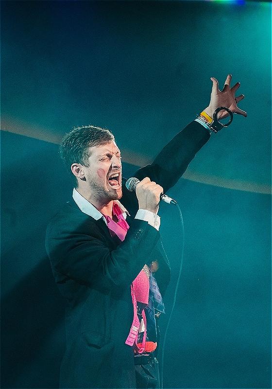 Jack Tucker shouting into a microphone with a lipstick stain on his cheek.