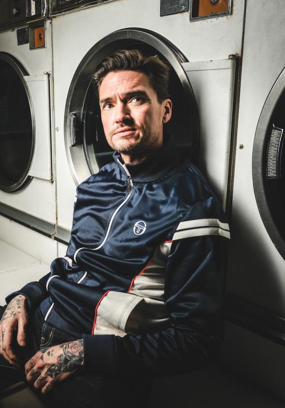 Jack sits in front of three launderette-style washing machines, looking upwards with a serious expression