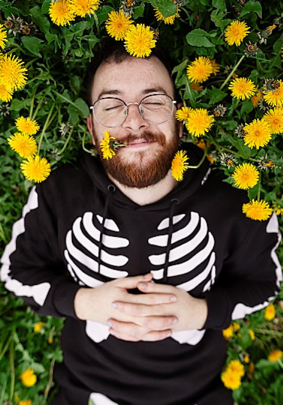 Rich Spalding lying in a field of dandelions wearing a skeleton jumper.