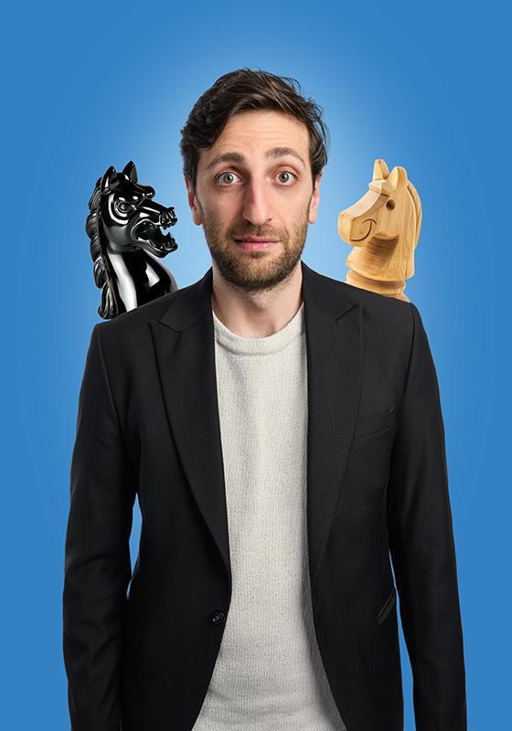 Vlad stands with two knights from a chess board perched on either shoulder. One black and one white, one looking kind and the other looking angry.