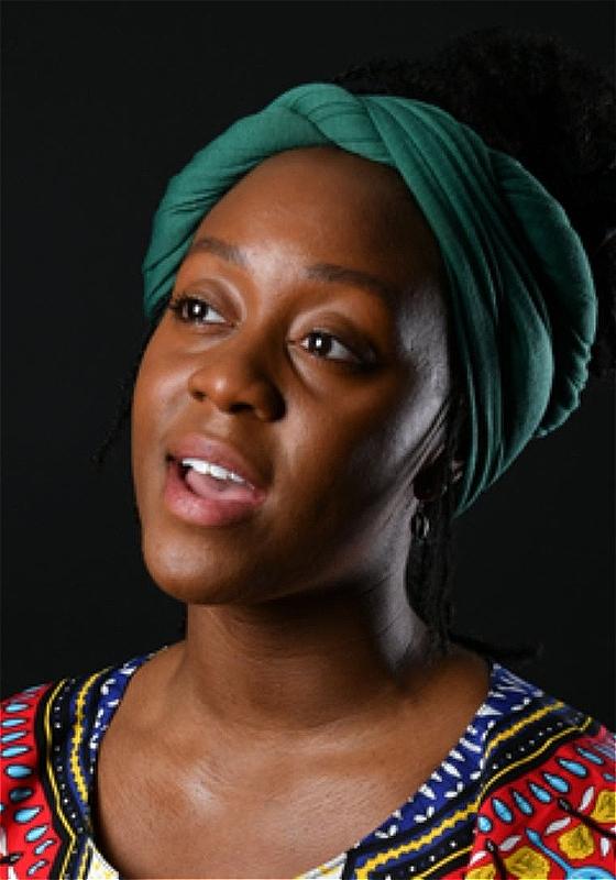 Portrait of a Black woman with a green headscarf and multicolored African print dress looking up and to the side, against a dark background.