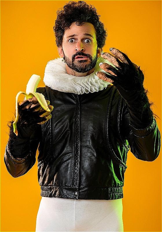 Man with curly hair looking surprised while holding a banana, wearing a black leather jacket and a white ruffled Elizabethan collar, with furry, gorilla-like hands against a yellow background.