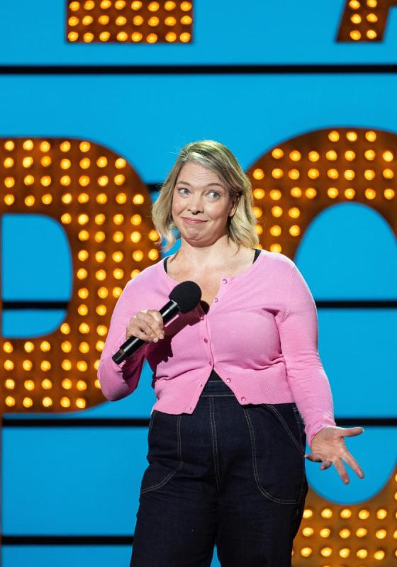 Spring Day in a pink cardigan and black trousers stands against the famous Live At The Apollo background. 