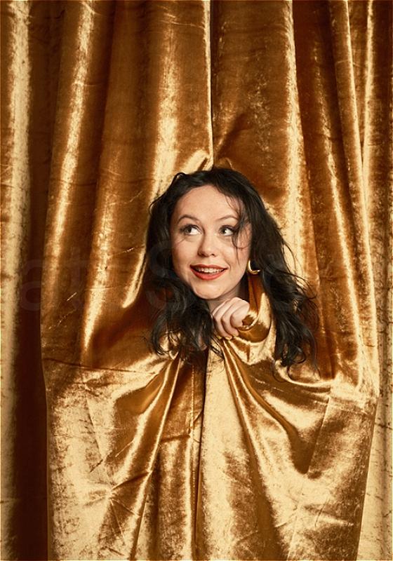 Amy Annette poking her head through a gold curtain