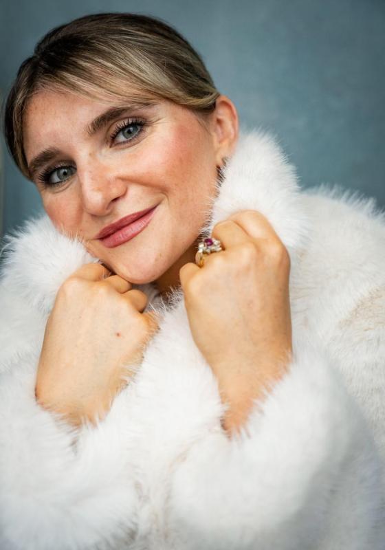 Sophie smiles at the camera wearing a cozy white fluffy jumper and a sparkly ring. Their hands are snuggled up towards their chin.