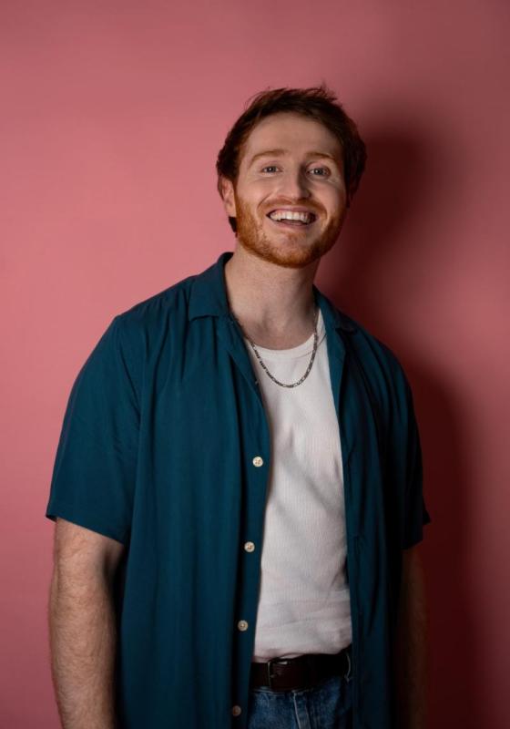 Ali smiling at the camera against a pink backdrop