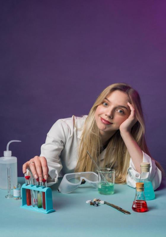 Freya smiles at the camera wearing a lab coat and surrounded by scientific apparatus