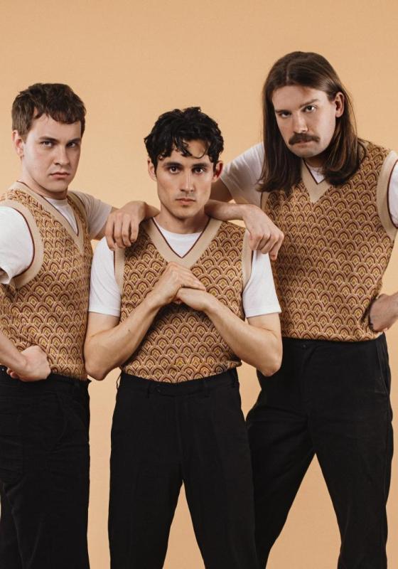 The cast of Crybabies wearing matching patterned sweater vests and black trousers looking menacingly at the camera.