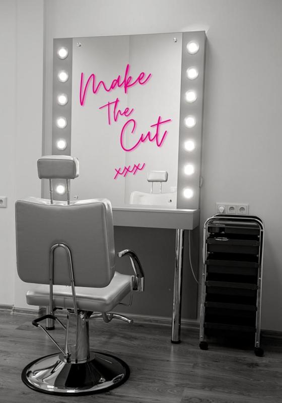 Black and white image of a makeup chair and makeup mirror with lights around it. The words 'Make The Cut xxx' are written in pink on the mirror/ 