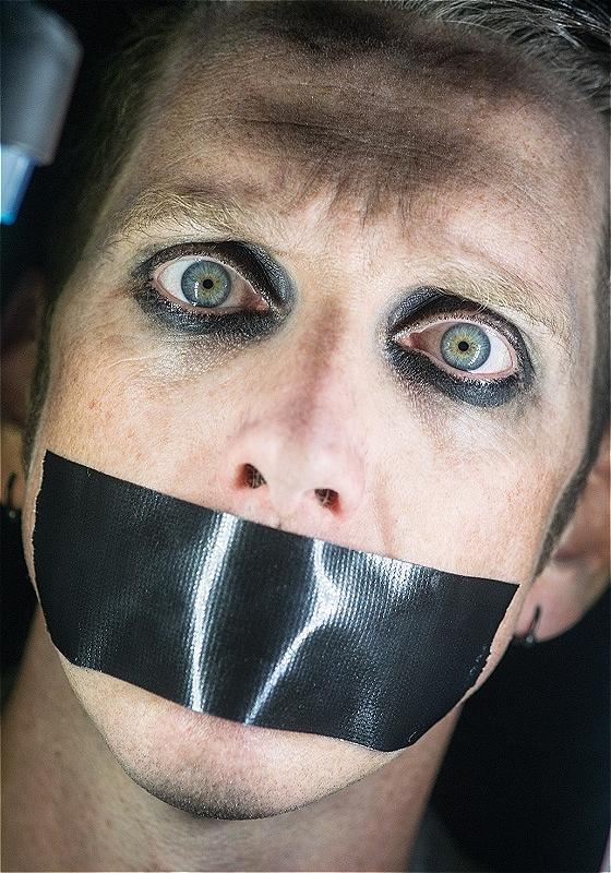 Tape faces head surrounded by lights. Thick black eye liner on & black tape over their mouth.