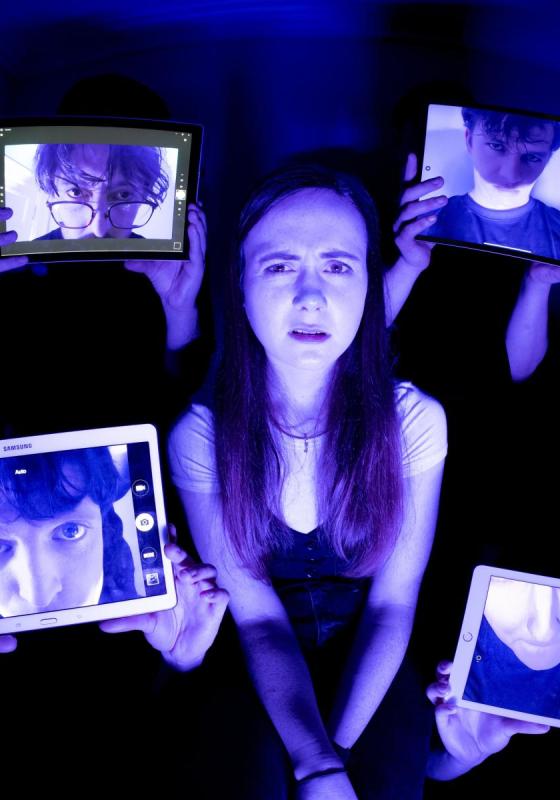 A girl with a bewildered expression surrounded by 4 screens with men's faces on under a backlight