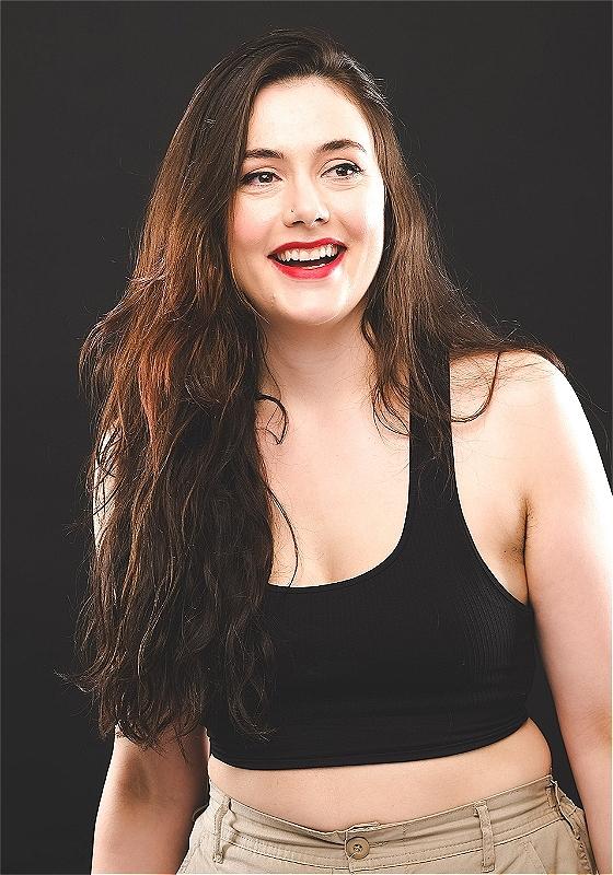 Marjolein laughingly looks over to the right, they have long brown hair and are wearing a black tank top. 