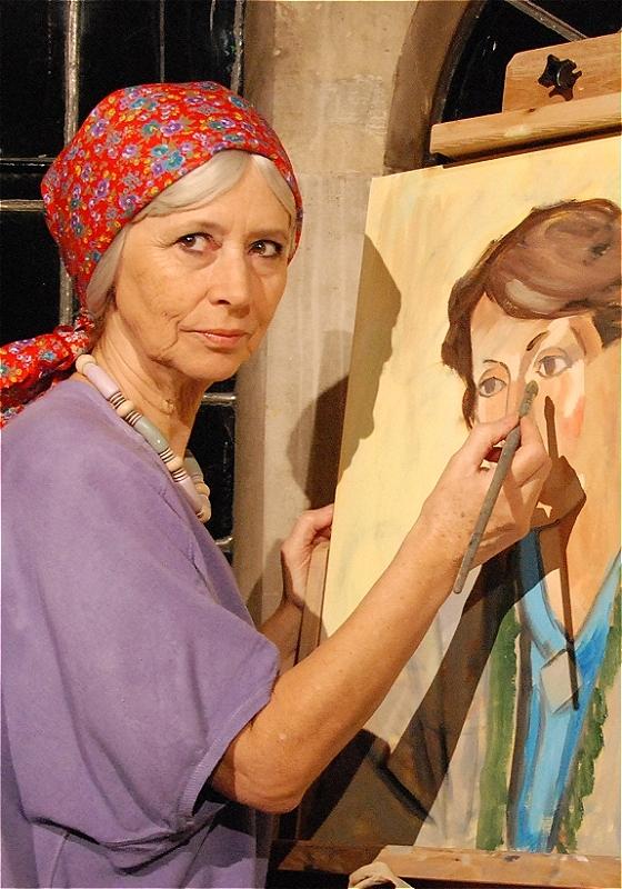 The actor applies the final details to a painting wearing a floral patterned headscarf.