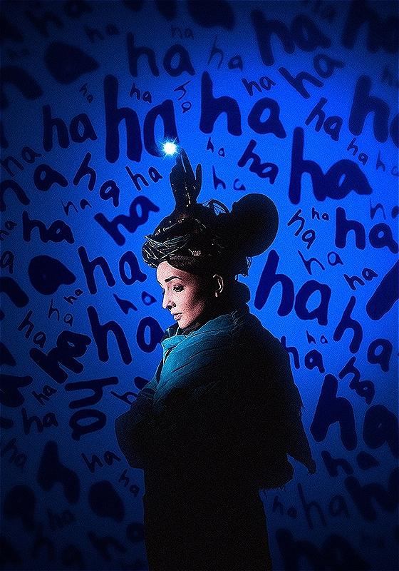 A woman standing in front of a blue background with 'ha ha ha' text. 