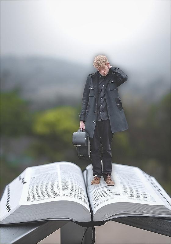 Callum stands on an open bible against a misty background, holding a guitar case and looking contemplative.