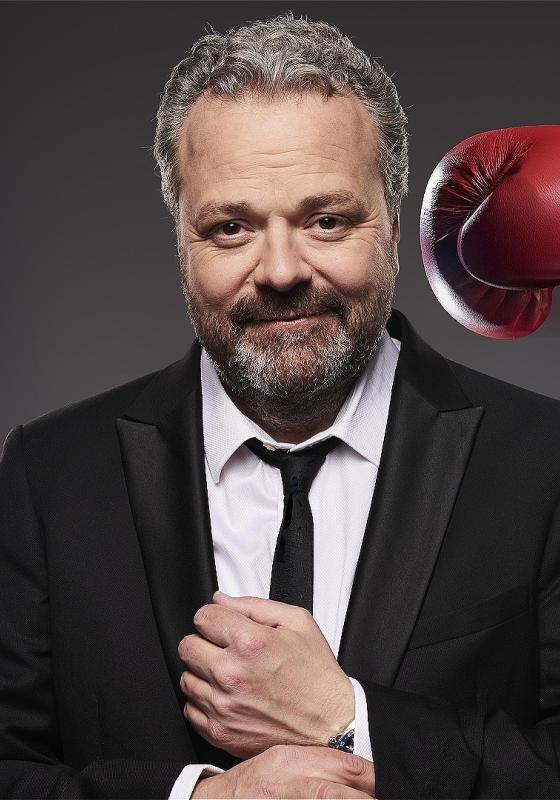 Hal in a black suit and tie, fixing his cuff link while a red boxing glove appears threateningly to his left. 