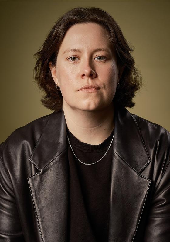 A headshot of Chloe Petts wearing a leather jacket and brown t shirt.