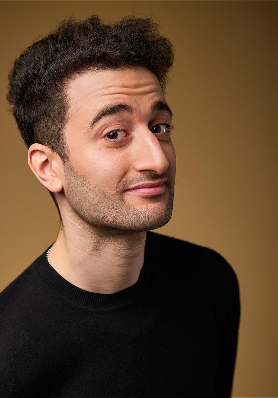 Hasan Al-Habib in a black shirt on a brown background, smiling at the camera