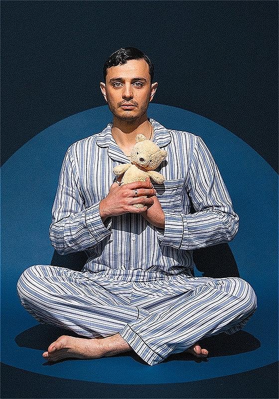 Pedro in blue and white striped pajamas sits cross-legged, holding a stuffed animal against a dark blue backdrop.