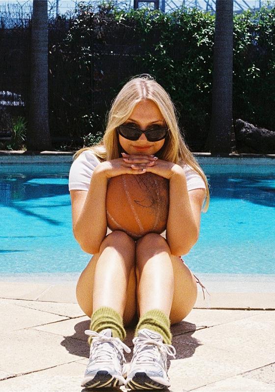 Jodie sits by the pool in sunglasses, resting her head on her hands.