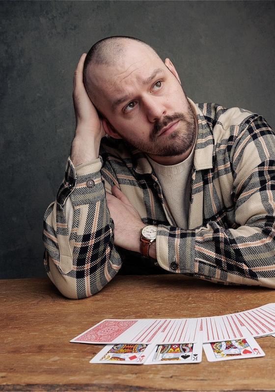 Andrew Frost in a flannel, leaning on his arm over a deck of cards