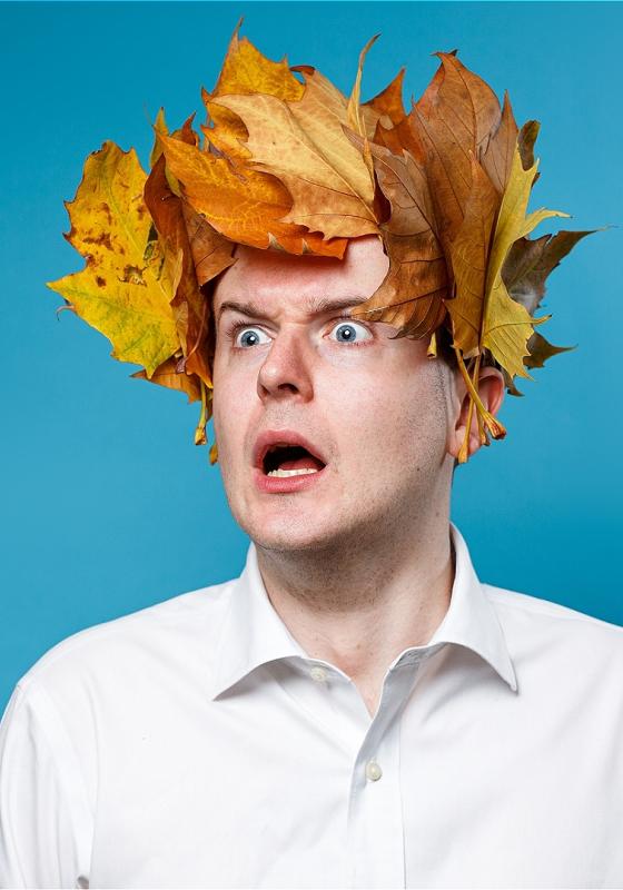 A shocked man on a blue background, wearing a crown of autumn leaves. 