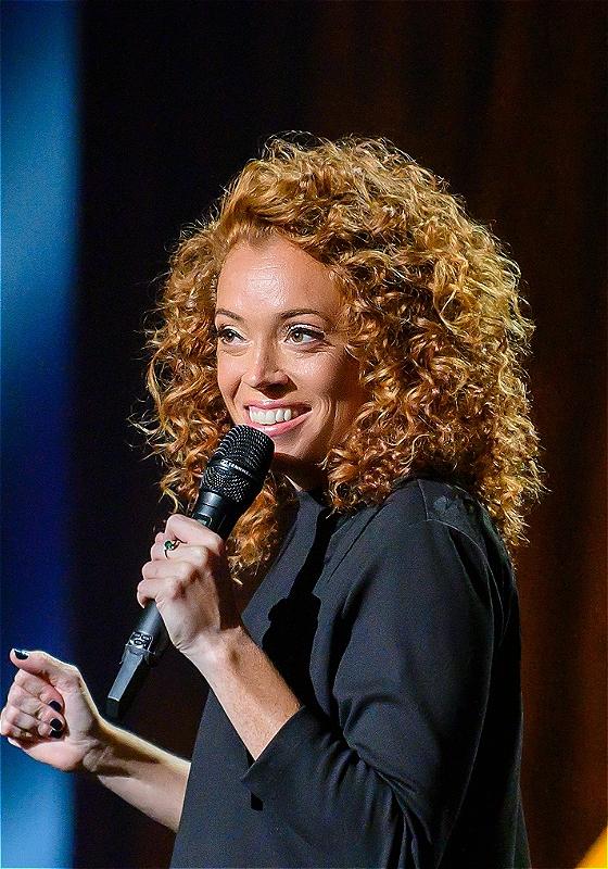 Photo of Michelle Wolf on stage holding a microphone.