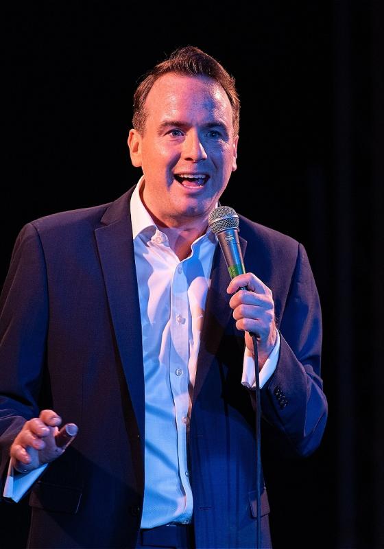 Matt in a relaxed suit speaking into a handheld mic