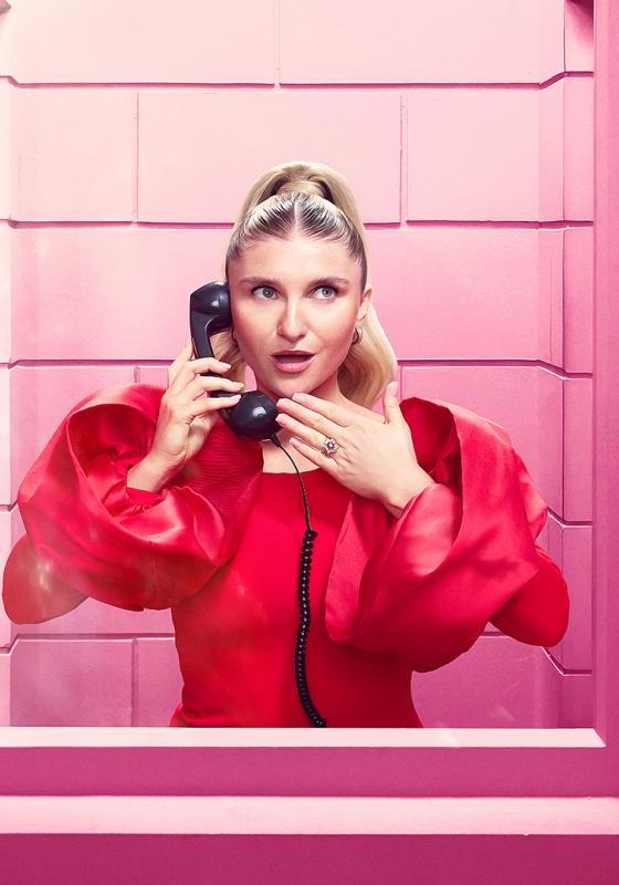 Sophie dressed in hot pink, in a pink phone booth, gasping as she holds a phone receiver. 