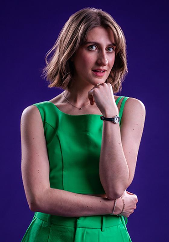 Anna wearing a green dress resting her chin on her hand subtly smiling at the camera.