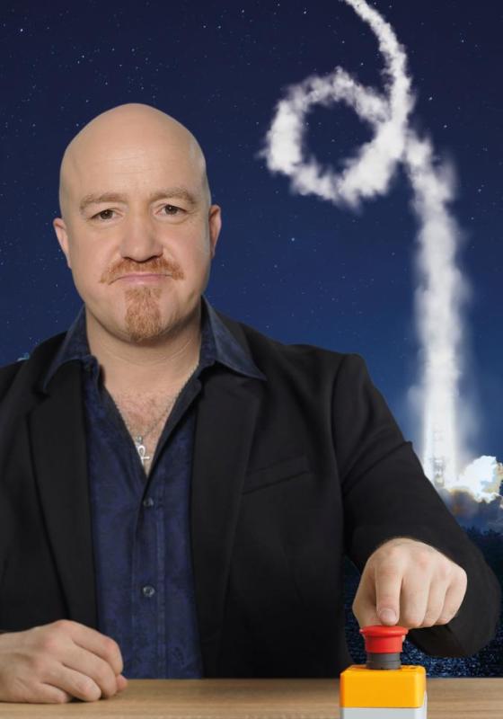 Andy holds his finger next to the big red button with smoke from a rocket appearing behind.